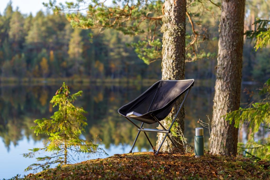 Beautiful forest lake with camping folding chair, book and vacuum insulated bottle.