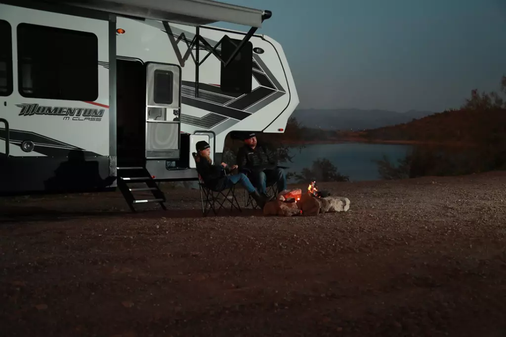 Daughter and dad sitting around a campfire with a Grand Design Momentum in the back. 