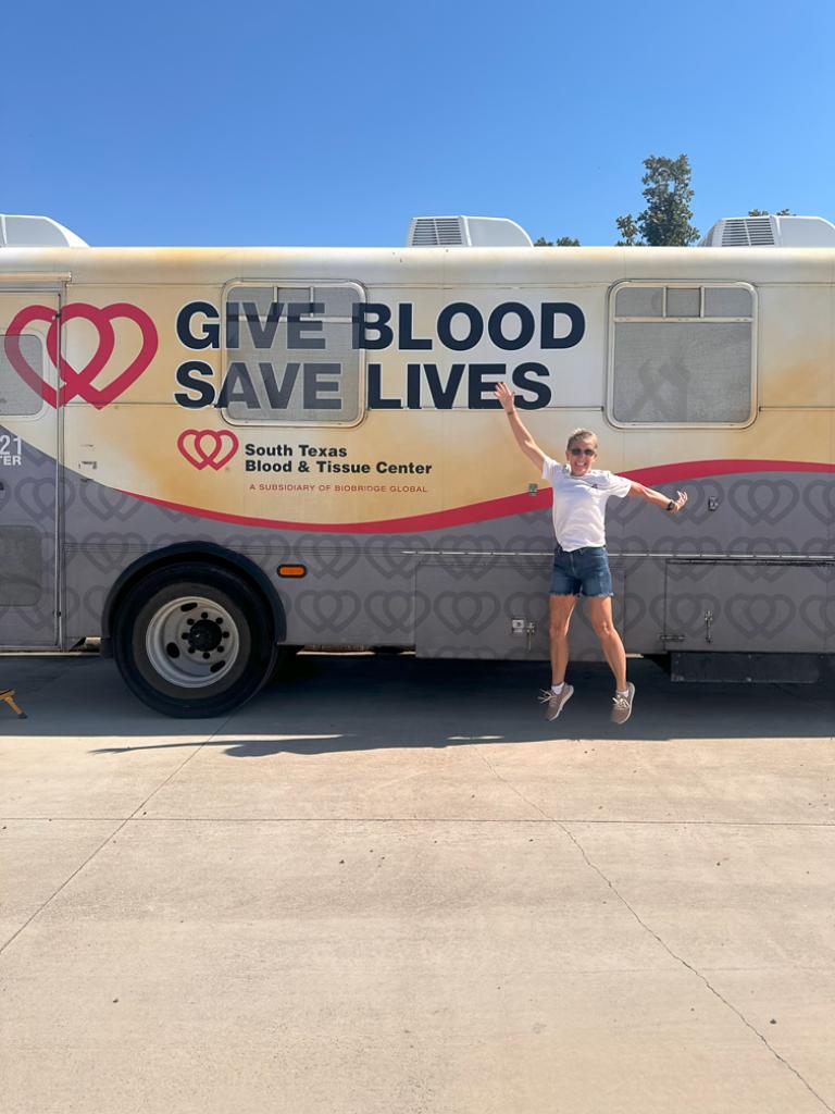 Impact team member in front of a "give blood saves lives" bus