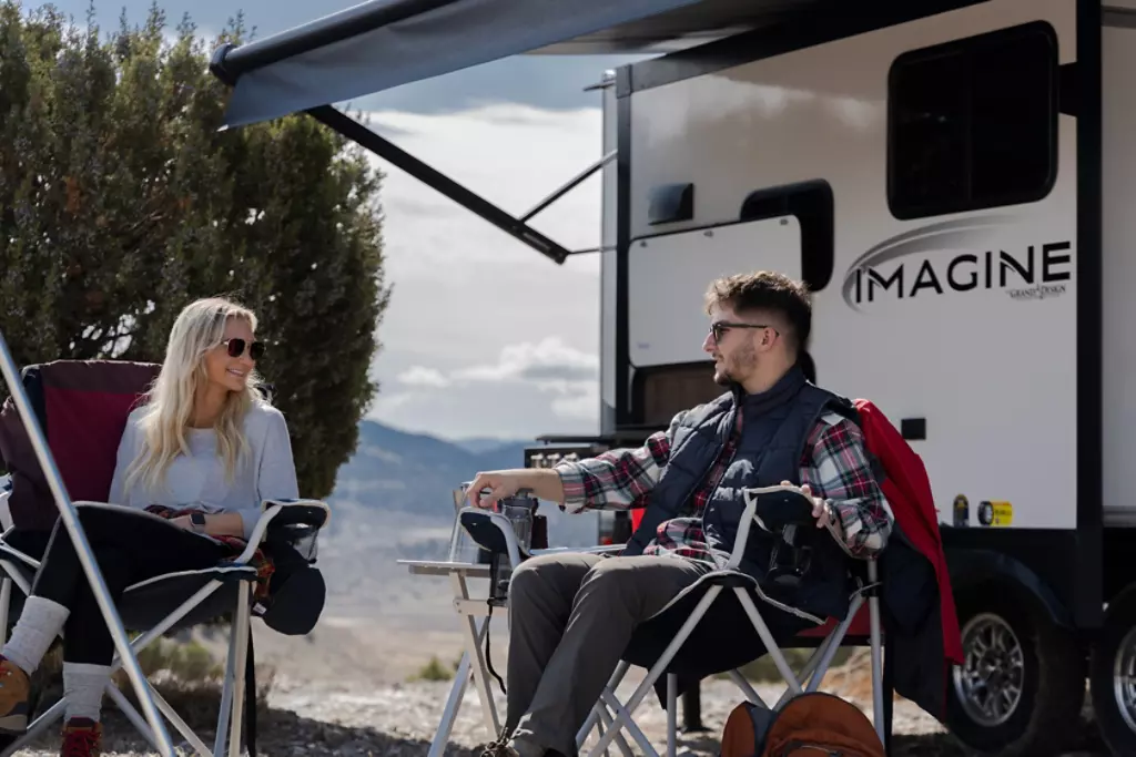 Couple sitting in camping chairs in front of a Grand Design Imagine. 