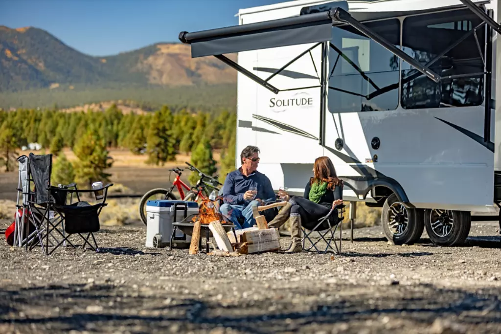 Family sitting around a fire in front of a Grand Design Solitude.