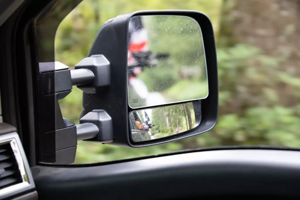 Extended rear view mirror with a blurry reflection of a dog sitting in the backseat of a truck. 